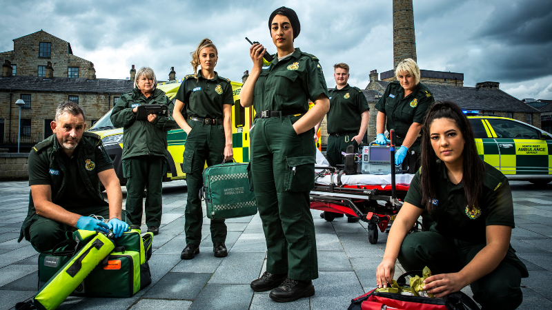 Ambulance crew staff pictured in green uniforms next to emergency service vehicles