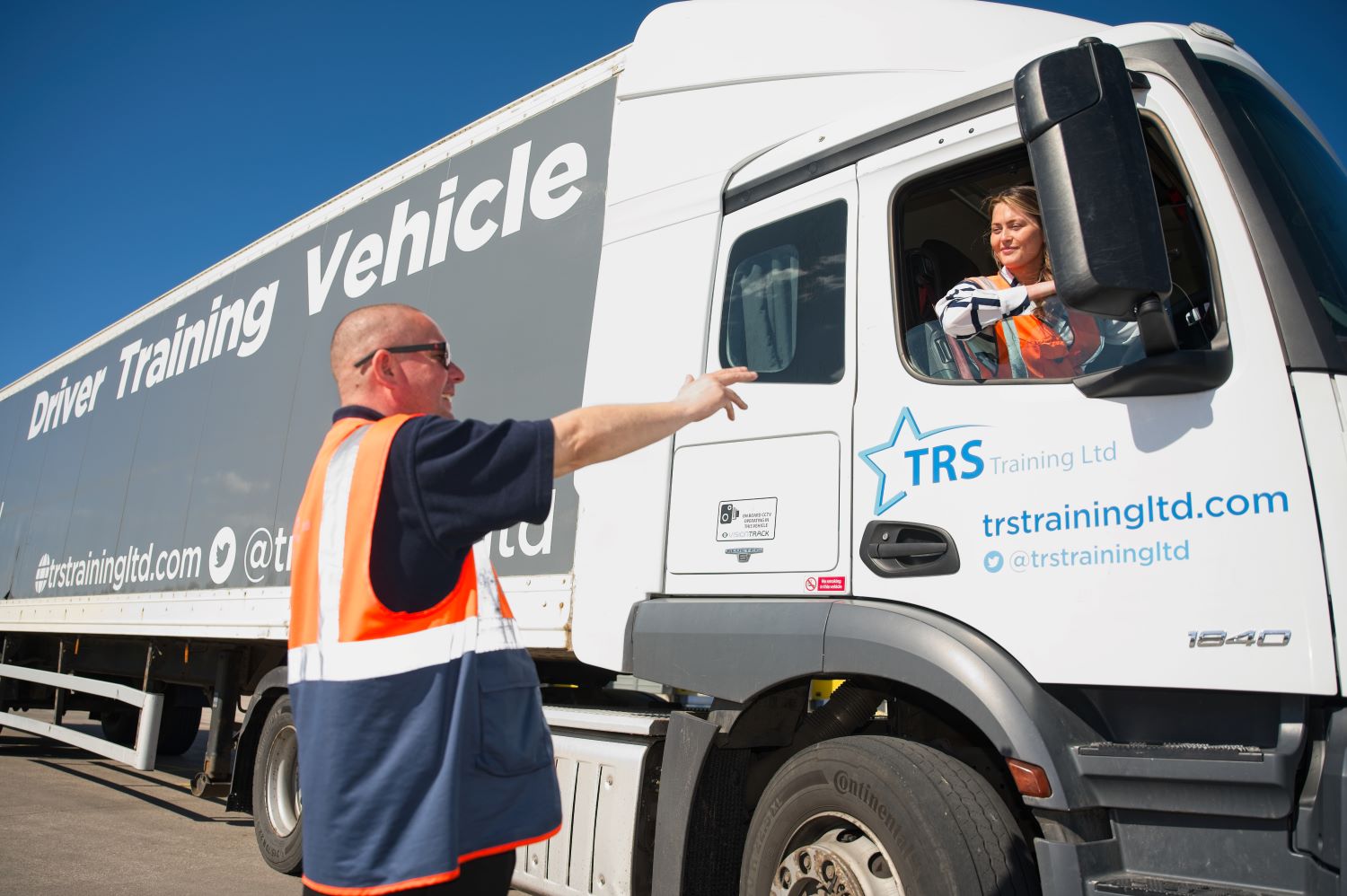 Female apprentice in truck driver cabin with tutor outside giving instructions